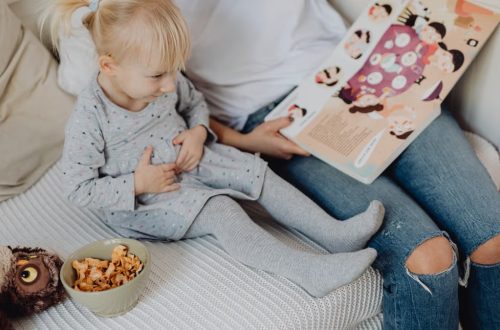 Mother reading a book to her daughter in a cozy bedroom setting with snacks nearby.