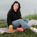 Woman enjoying a peaceful moment by the lake with a yoga mat and water bottle, promoting wellness.